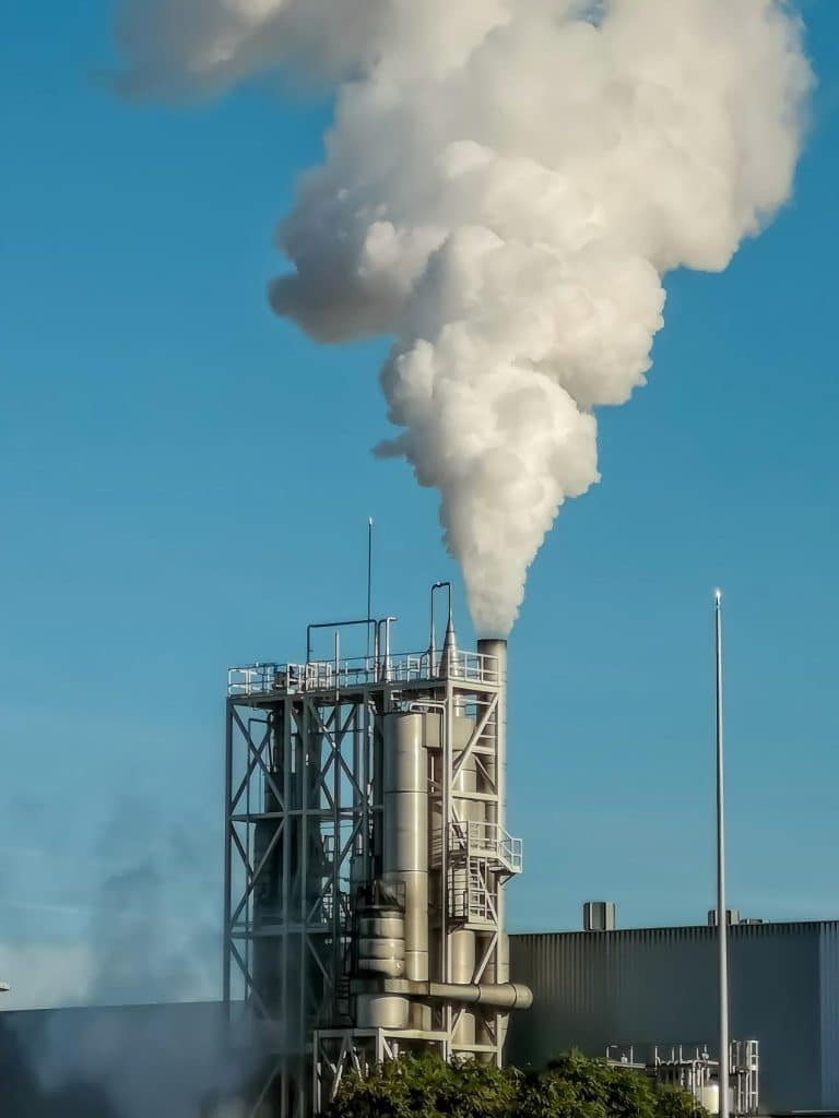 Industrial chimneys are releasing a large amount of smoke into the blue sky.